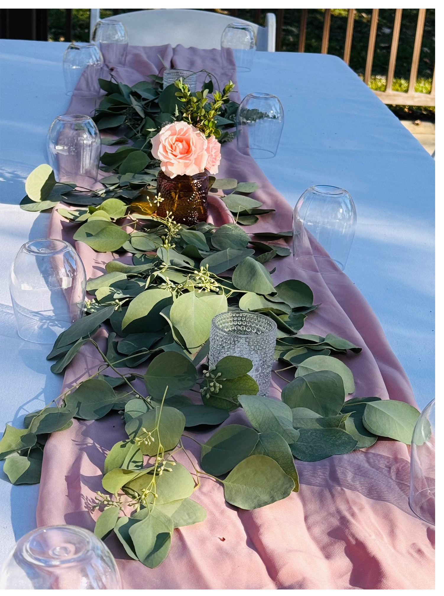 Close-up of an elegant wedding table setting featuring floral arrangements, a pink table runner, and glassware.