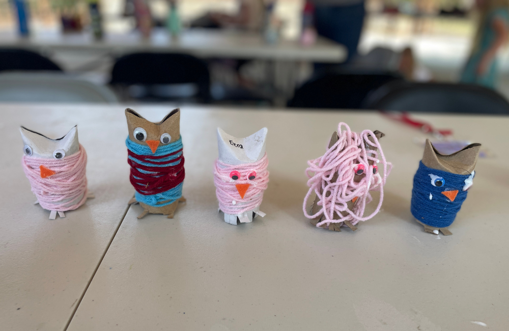 Five owls, crafted out of cardboard, yarn and google eyes, sitting in a row.