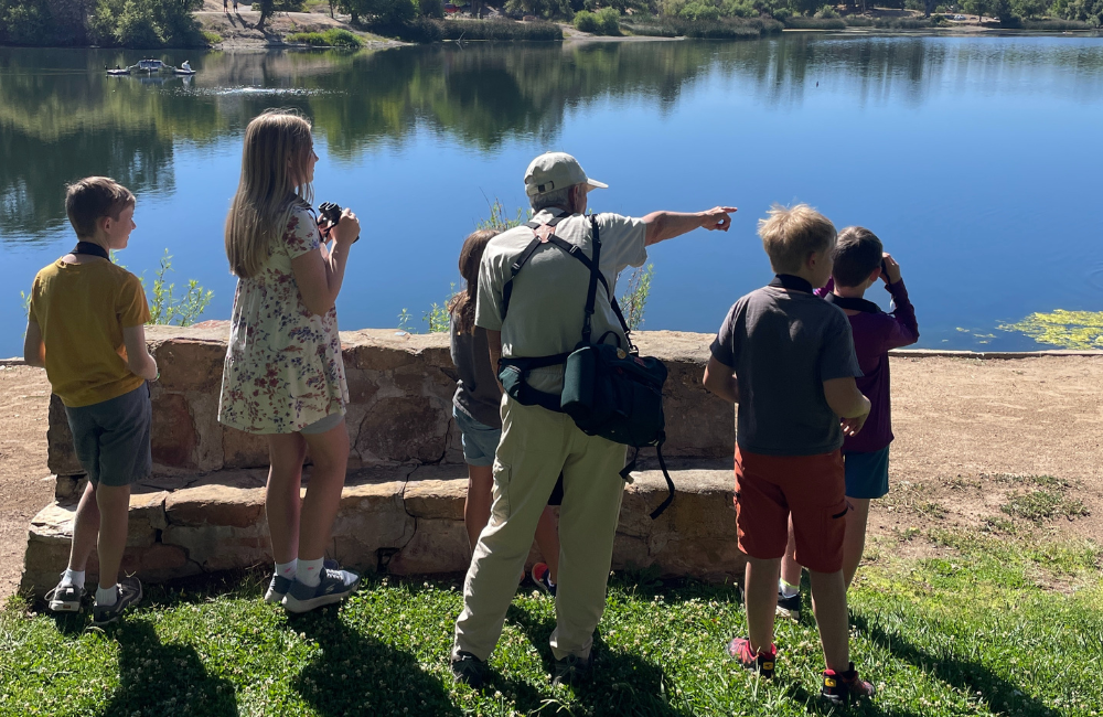 Group of children and instructor looking out at Atascadero Lake with binoculars.