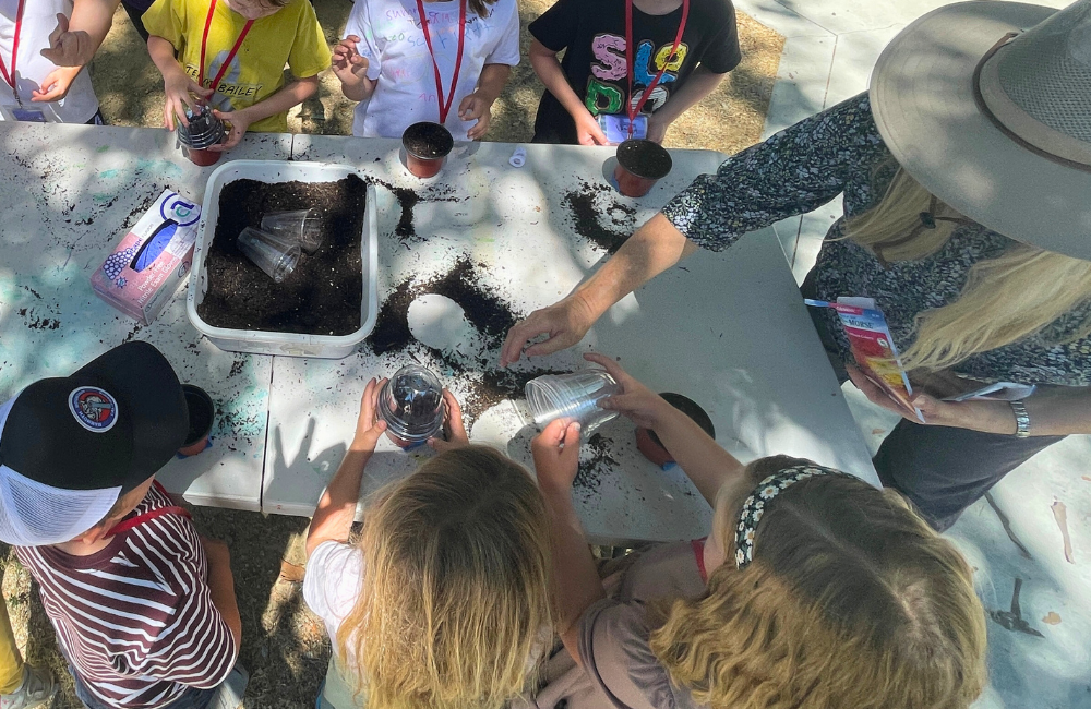 Shot from above, looking down on kids and an instructor standing around a table working with dirt/po